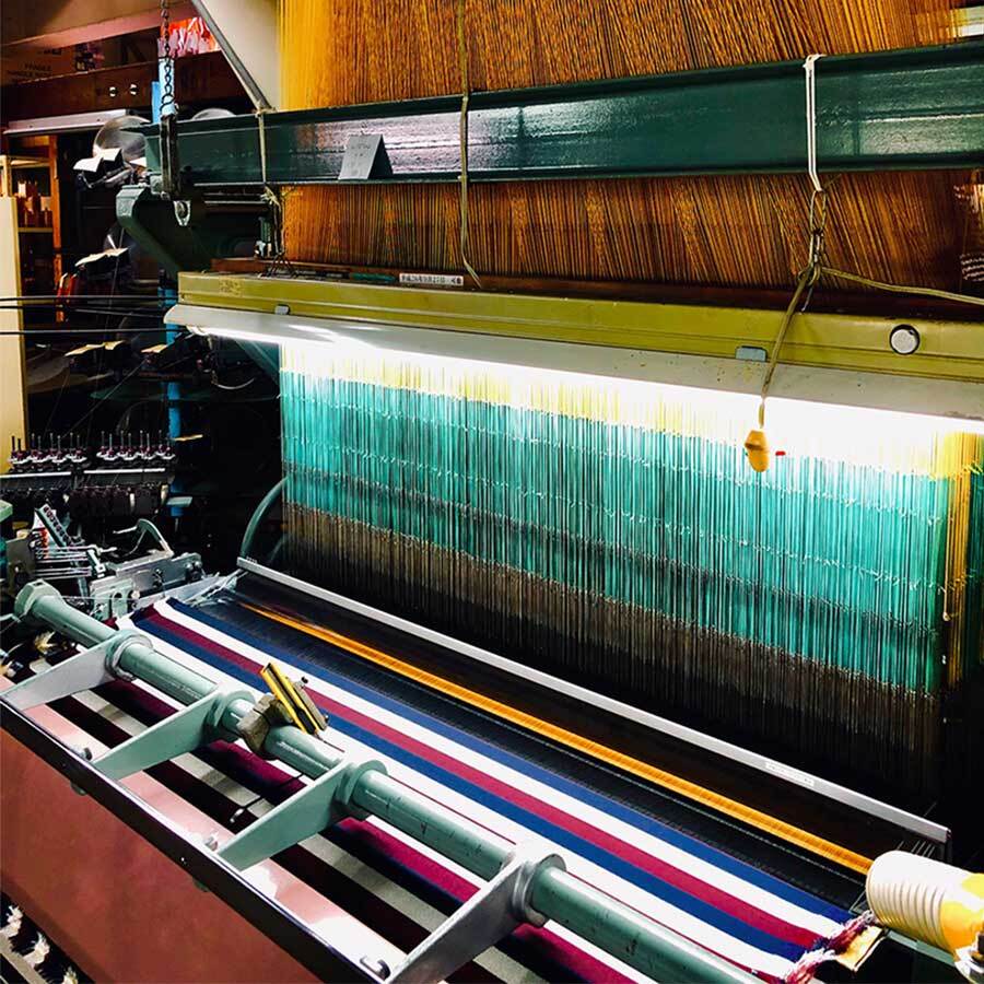 昔ながらの紋紙を使って織る織機です、織り上がった生地は手前で巻かれていきます